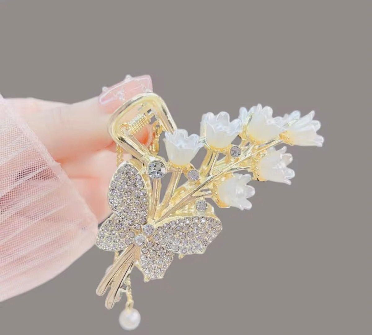 Tulip Blanc Isabella design: gold-tone hair claw with a sparkling butterfly, white tulip-shaped flowers, and a single pearl-style drop, displayed in hand.