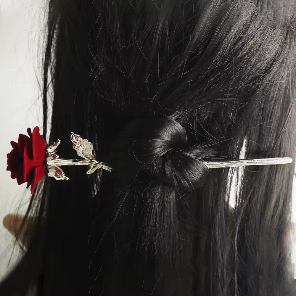 Red velvet rose hair stick with a silver-tone floral stem securing a twisted bun in long black hair.