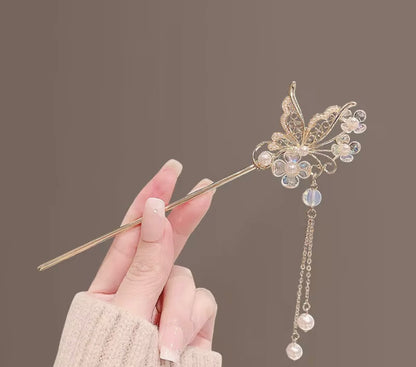 Elegant gold-tone butterfly hair stick adorned with sparkling wings, iridescent floral accents, and dangling pearl-like beads.