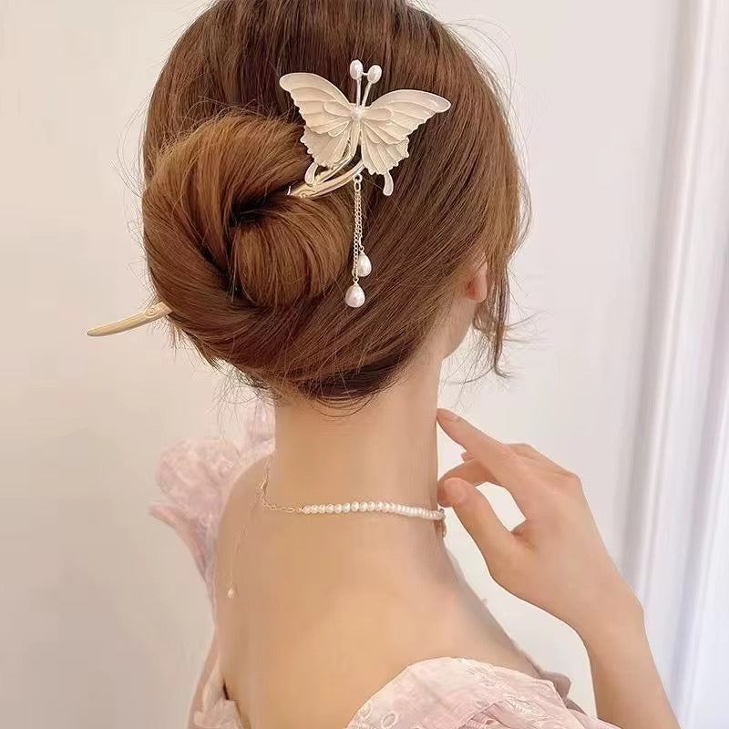 Ivory butterfly hair stick securing an elegant twisted bun, featuring decorative wings and dangling pearl-like accents.