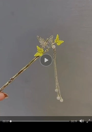 Video showcasing a gold-tone butterfly hair stick with sparkling crystal-like wings, two delicate yellow butterflies, and dangling pearl-like accents that sway gently with movement.