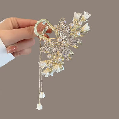 Tulip Blanc Juliette design: gold-tone butterfly hair claw with a pearl-style center, sparkling wings, white tulip-shaped flowers, and two dangling floral charms, displayed in hand.