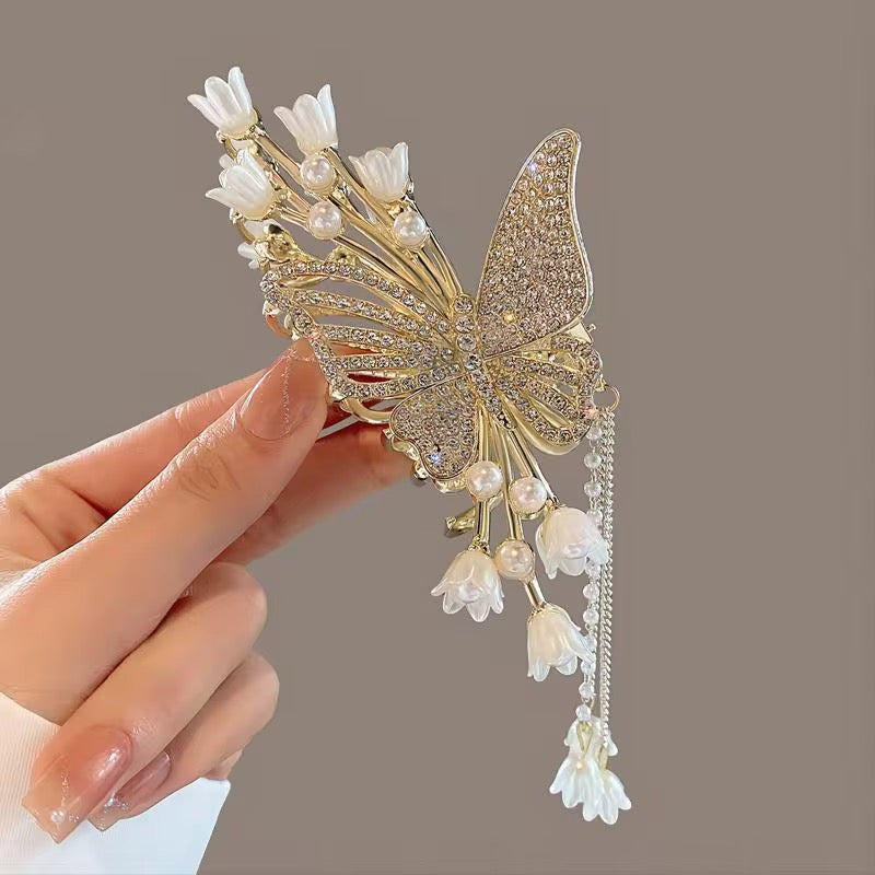 Tulip Blanc Lucia design: gold-tone hair claw with a large butterfly, openwork and sparkling wing details, white tulip-shaped flowers, and cascading floral drops, displayed in hand.