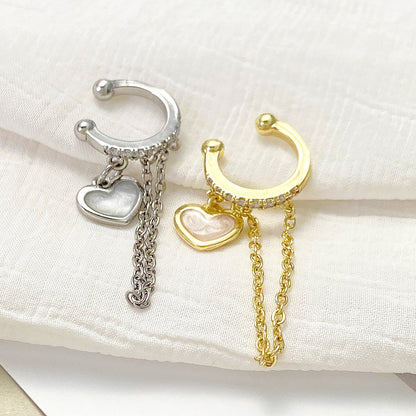 Two small hoop-style dangling earrings with heart charms, one silver-toned and one gold-toned, displayed on a soft white fabric surface.