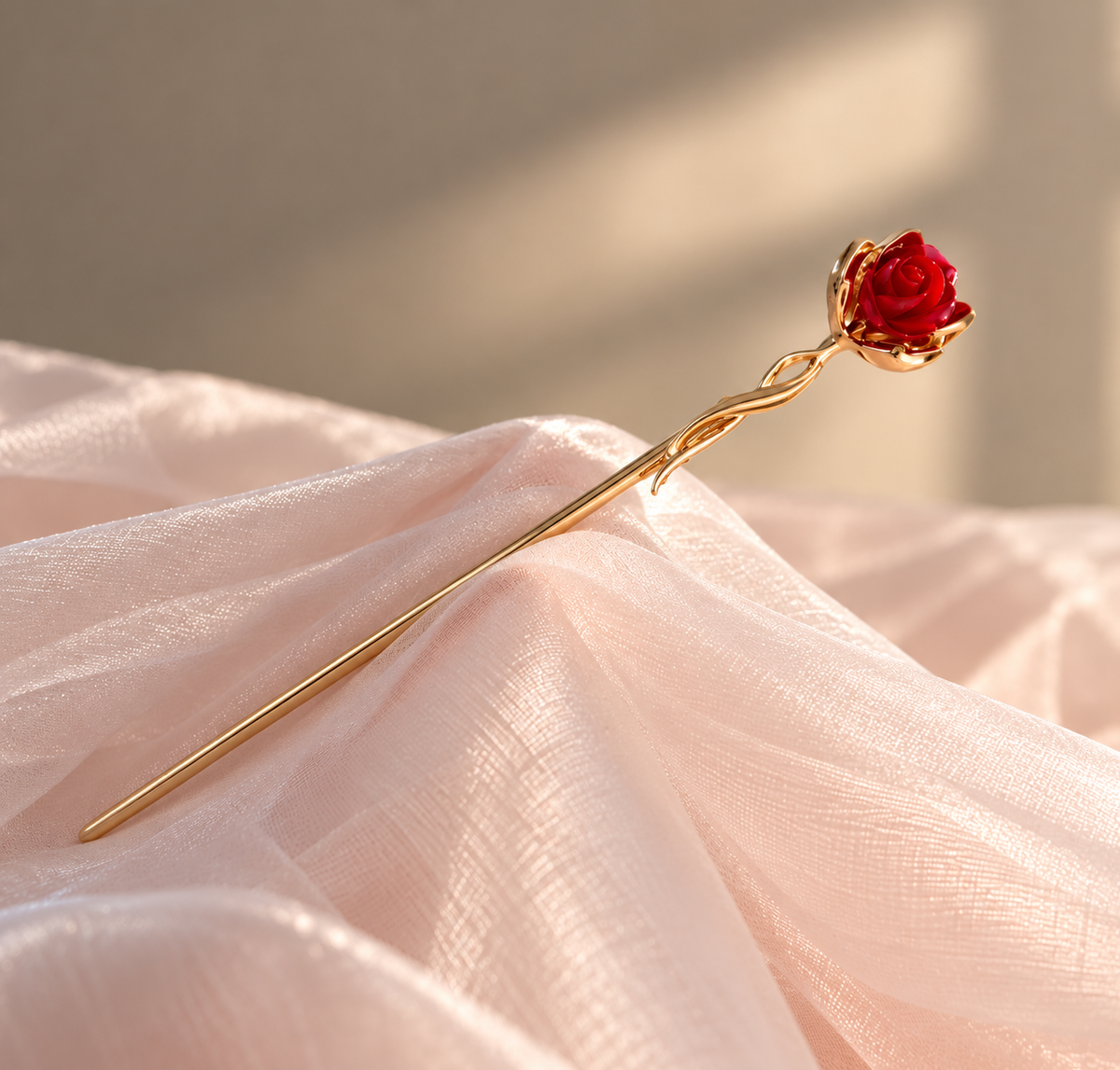Mini Rosita gold-tone hair stick featuring a small sculpted red rose and an elegant twisted stem, displayed on soft blush pink fabric.